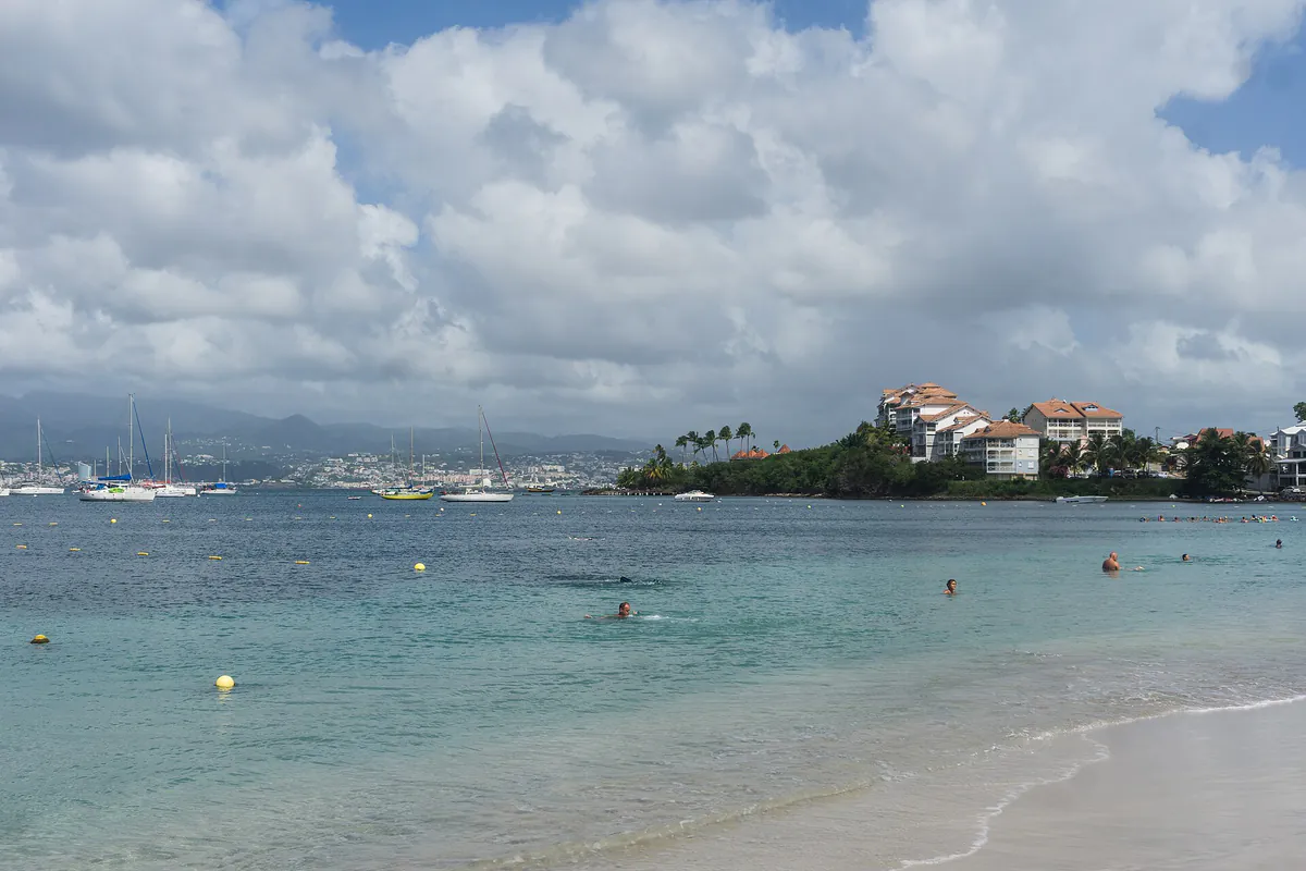 Front de mer du bourg des Trois-Îlets avec ponton, palmiers et reliefs de la baie